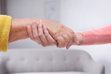 Photo of People holding hands together indoors. Help and elderly care service