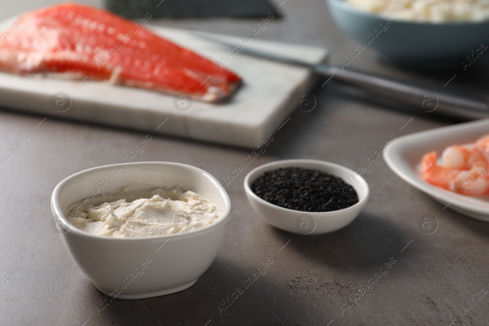 Photo of Cream cheese in bowl, sesame seeds and other ingredients for sushi on grey table, closeup