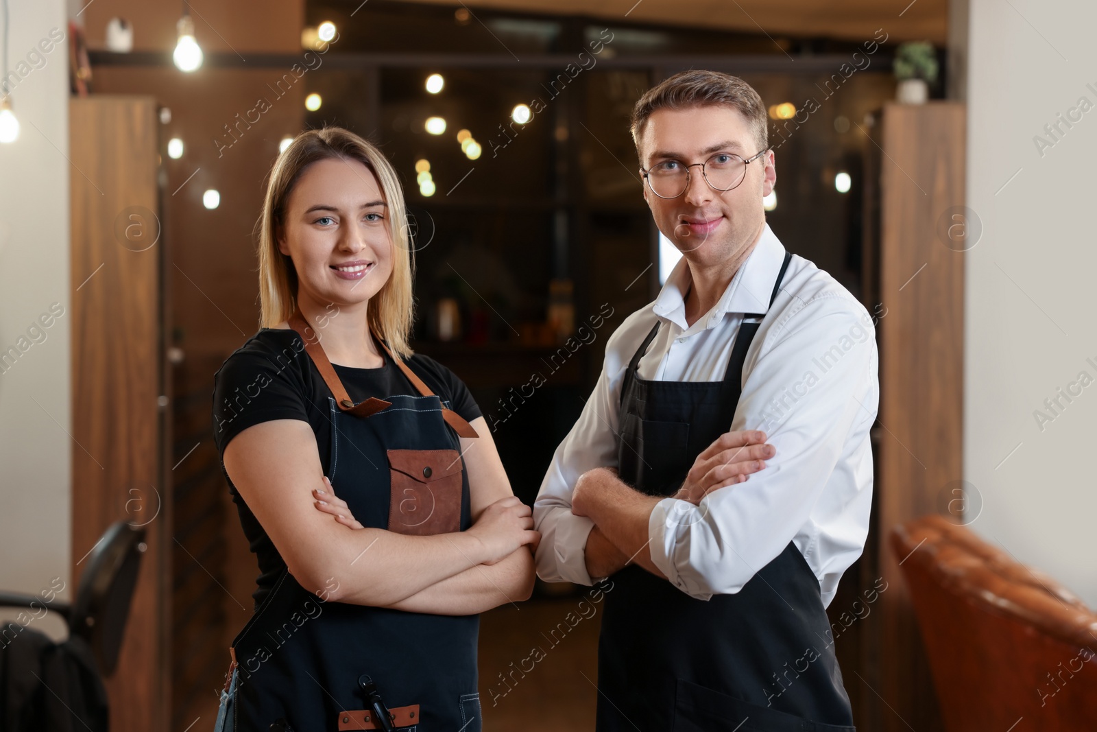 Photo of Portrait of professional hairdressers wearing aprons in beauty salon