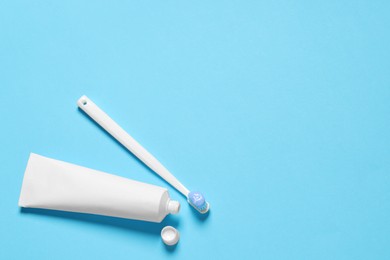 Photo of Plastic toothbrush with paste and tube on light blue background, flat lay. Space for text