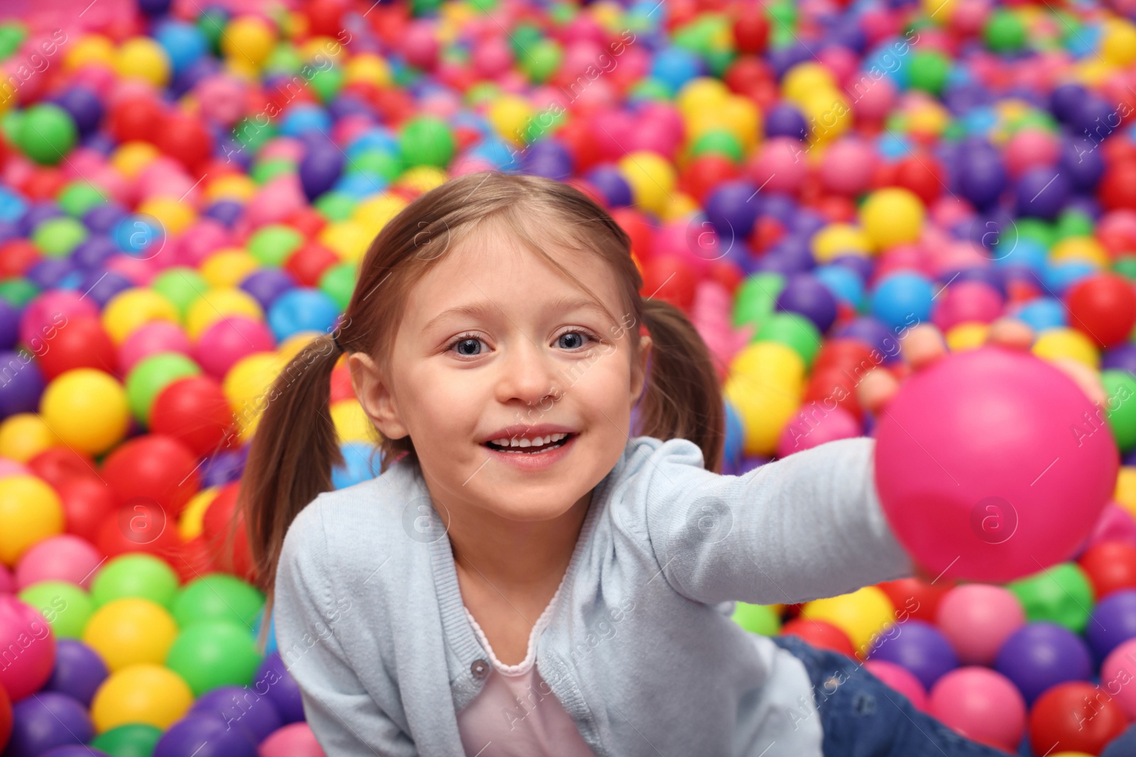 Photo of Happy little girl sitting on colorful balls in ball pit