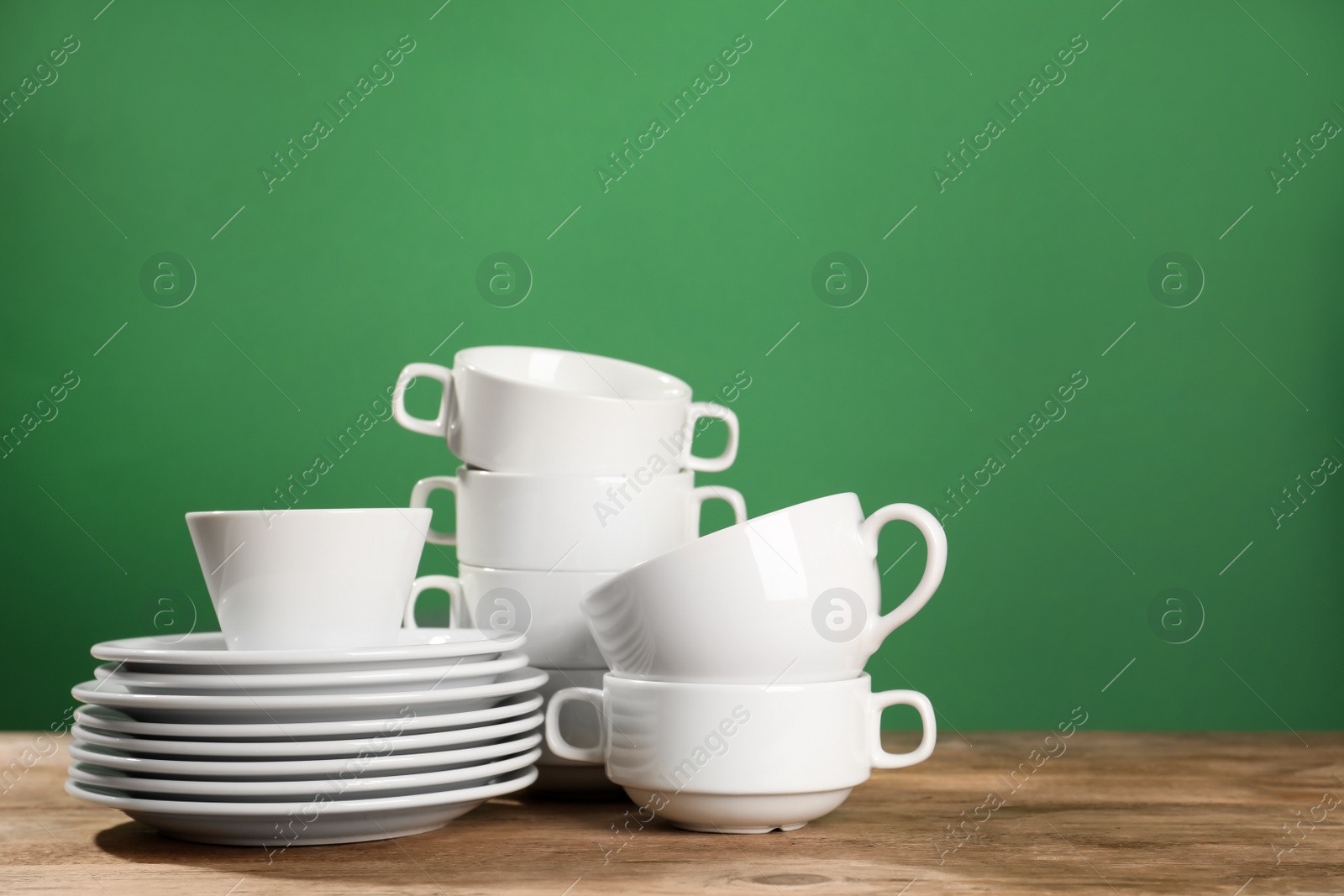 Photo of Set of clean dishware on wooden table against green background, space for text