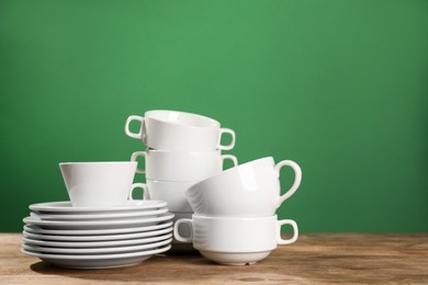 Set of clean dishware on wooden table against green background, space for text