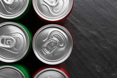 Photo of Energy drink in cans on black textured background, top view. Space for text