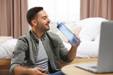 Man with transparent plastic bottle of water in bedroom at home