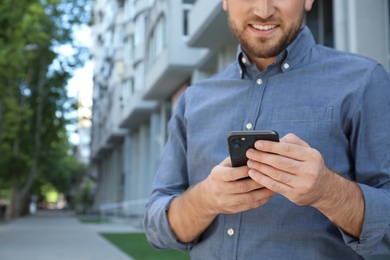 Young man with smartphone on city street, closeup