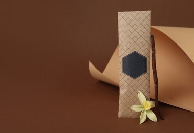Scented sachet, vanilla stick and flower on brown background, space for text