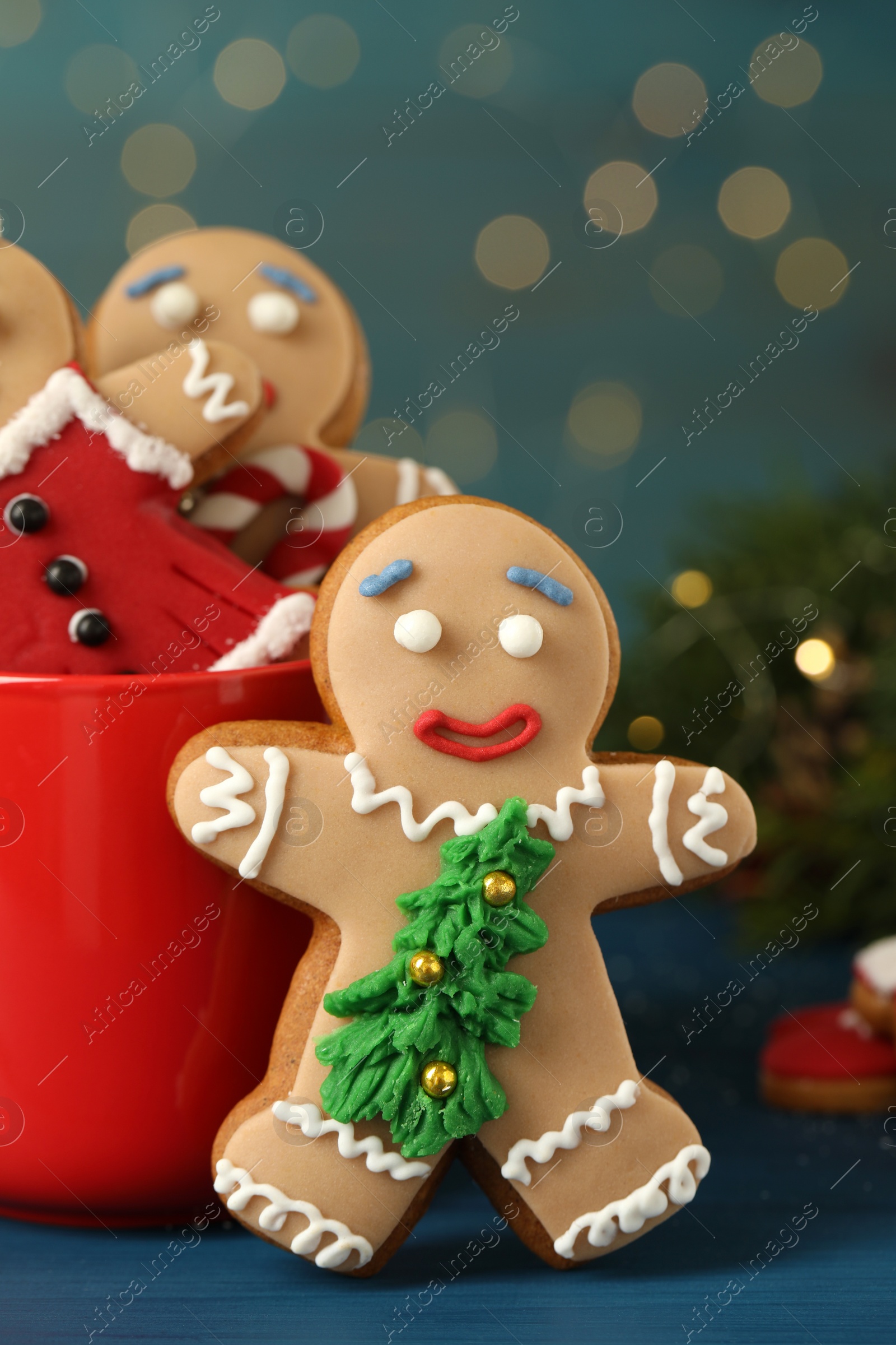 Photo of Delicious homemade Christmas cookies with cup on blue wooden table against blurred festive lights