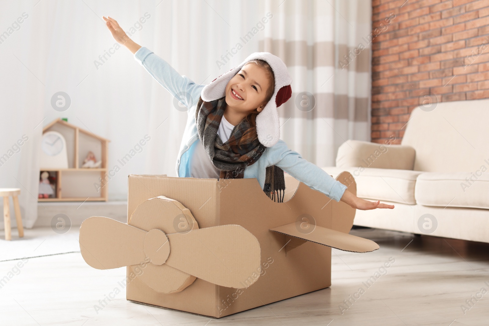 Photo of Cute little girl playing with cardboard airplane in living room