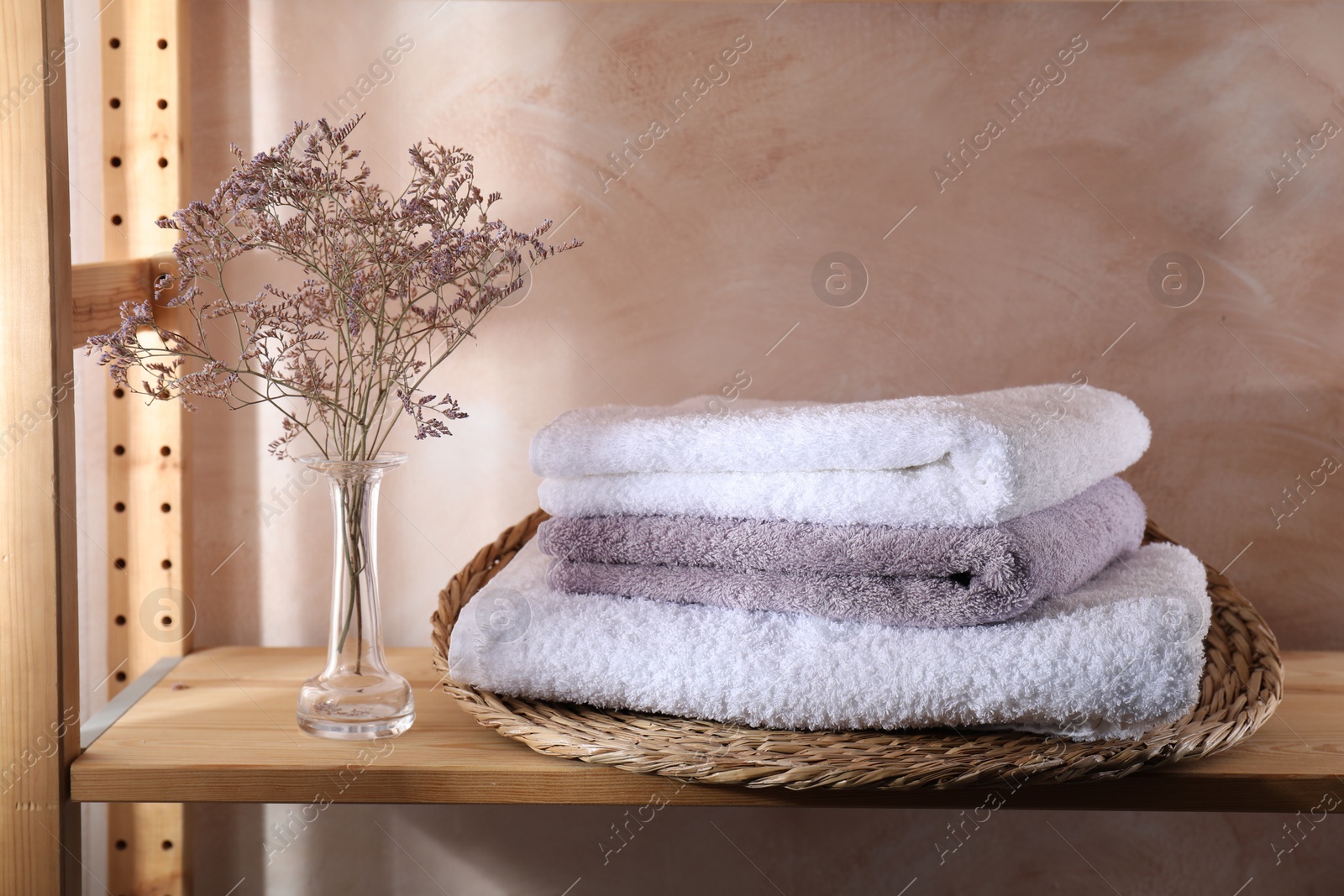 Photo of Stacked soft towels and flowers on wooden shelf indoors