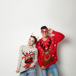 Couple in Christmas sweaters, deer headband and party glasses on white background