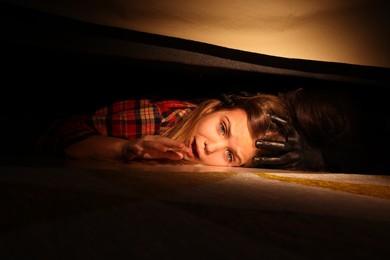 Childhood phobia. Little girl with monster under bed at home, closeup