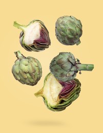 Image of Fresh raw artichokes falling on pale yellow background