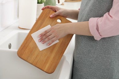 Photo of Woman wiping wooden cutting board with paper napkin at sink in kitchen, closeup