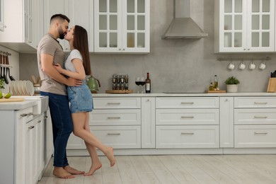 Photo of Affectionate couple kissing in kitchen. Space for text