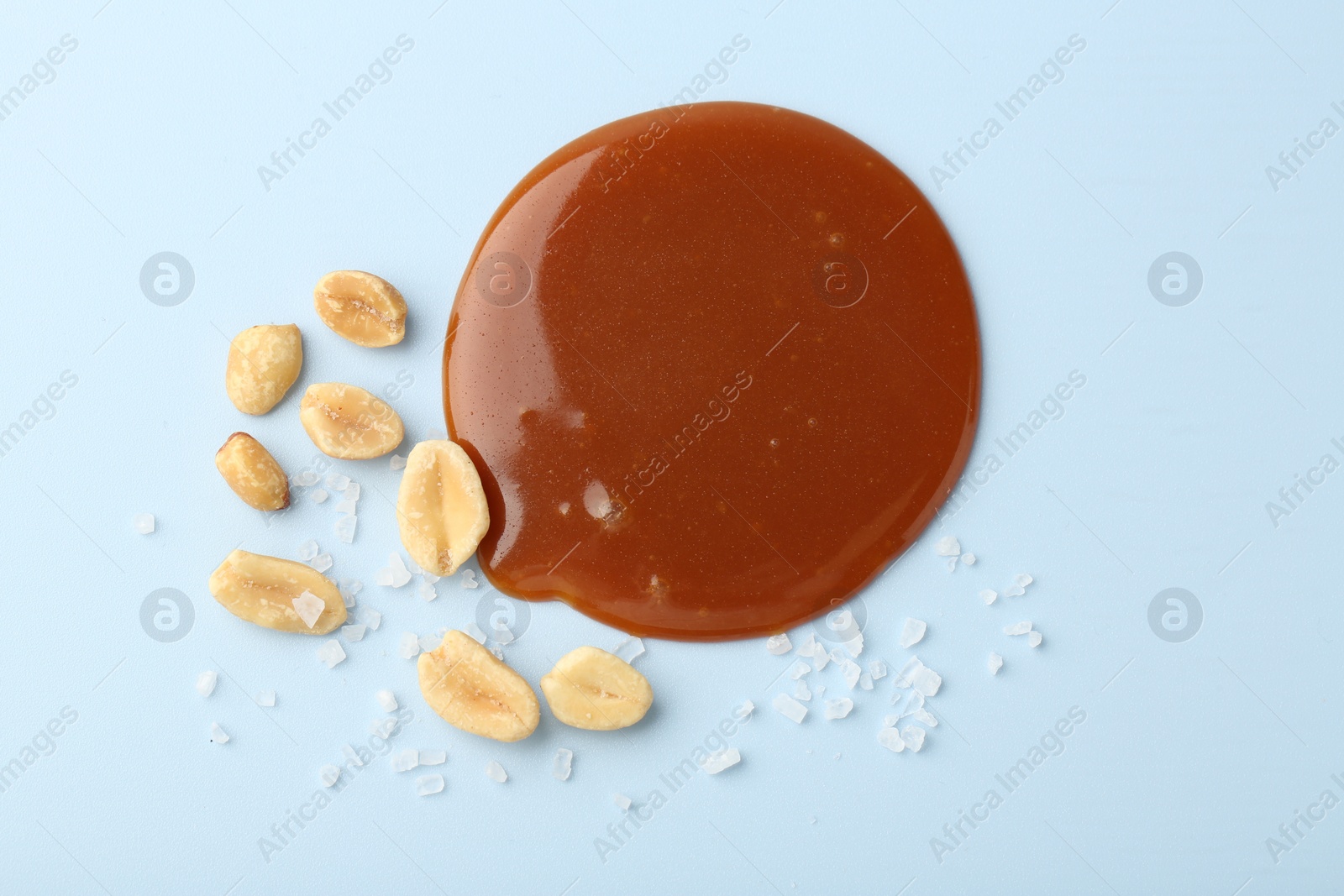 Photo of Smear of tasty salted caramel, peanuts and salt on light blue background, flat lay