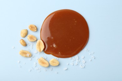 Smear of tasty salted caramel, peanuts and salt on light blue background, flat lay