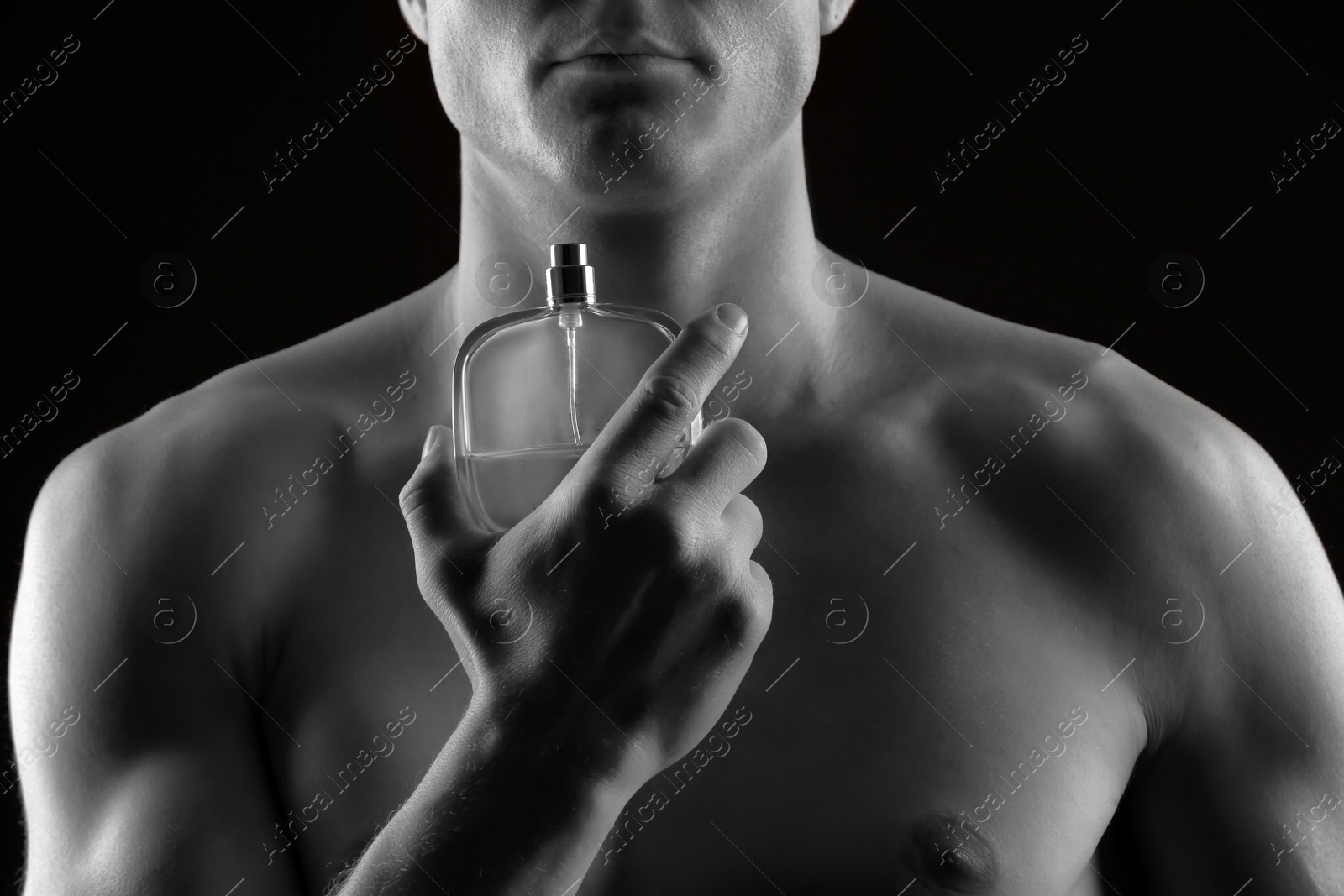 Photo of Handsome man using perfume on black background, closeup. Black and white effect