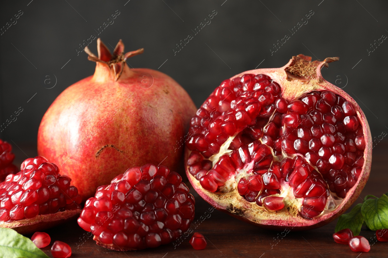 Photo of Fresh pomegranates and green leaves on wooden table, closeup