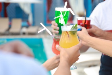 Friends clinking glasses with fresh summer cocktails near swimming pool, closeup