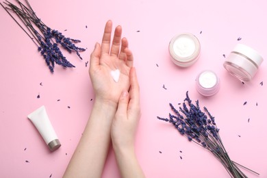 Photo of Woman applying hand cream and lavender flowers on pink background, top view