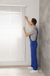 Worker in uniform opening or closing horizontal window blind indoors