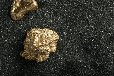 Photo of Shiny gold nuggets on black sand, above view. Space for text