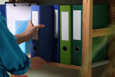 Photo of Woman taking binder office folder from shelving unit indoors, closeup