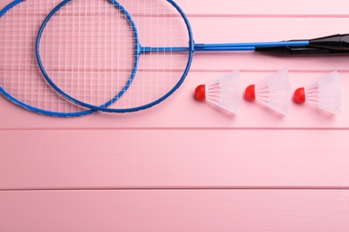 Photo of Badminton rackets and shuttlecocks on pink wooden table, flat lay. Space for text