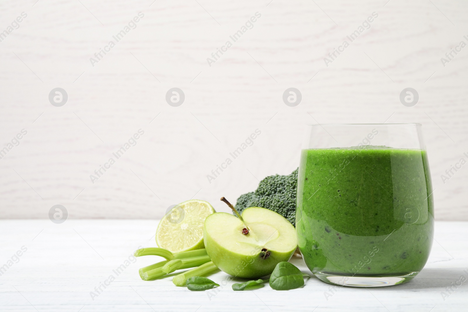 Photo of Delicious green juice and fresh ingredients on white wooden table, space for text