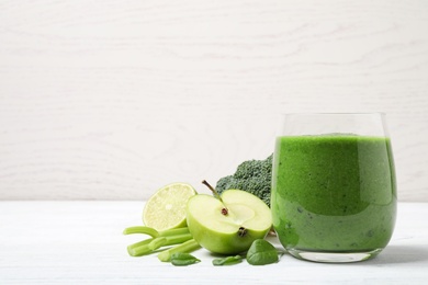 Delicious green juice and fresh ingredients on white wooden table, space for text