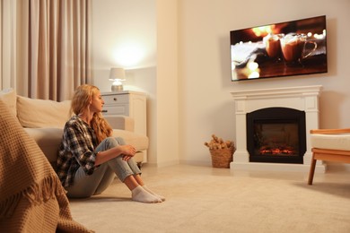 Photo of Beautiful young woman resting near fireplace at home