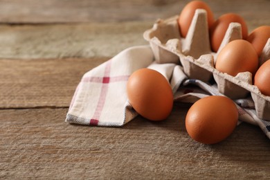 Raw chicken eggs with carton and napkin on wooden table, closeup. Space for text