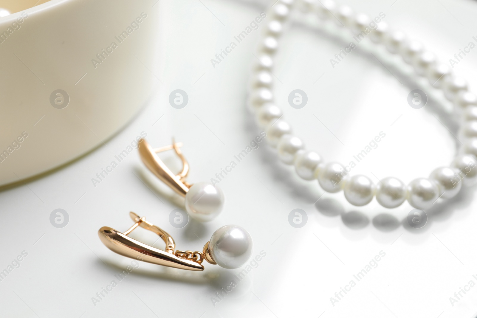 Photo of Elegant golden earrings and necklace with pearls on white table, closeup