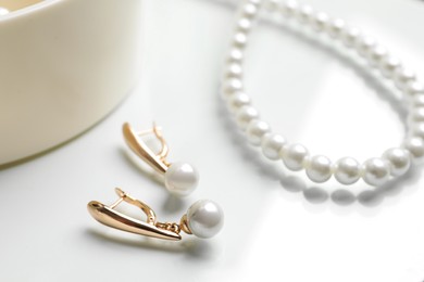 Photo of Elegant golden earrings and necklace with pearls on white table, closeup