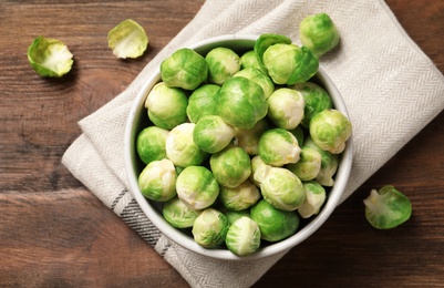 Photo of Bowl of fresh Brussels sprouts and napkin on wooden background, top view