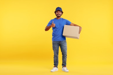 Happy young courier with parcel showing thumb up on orange background