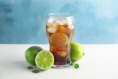 Glass of coke with ice cubes and limes on table against color background