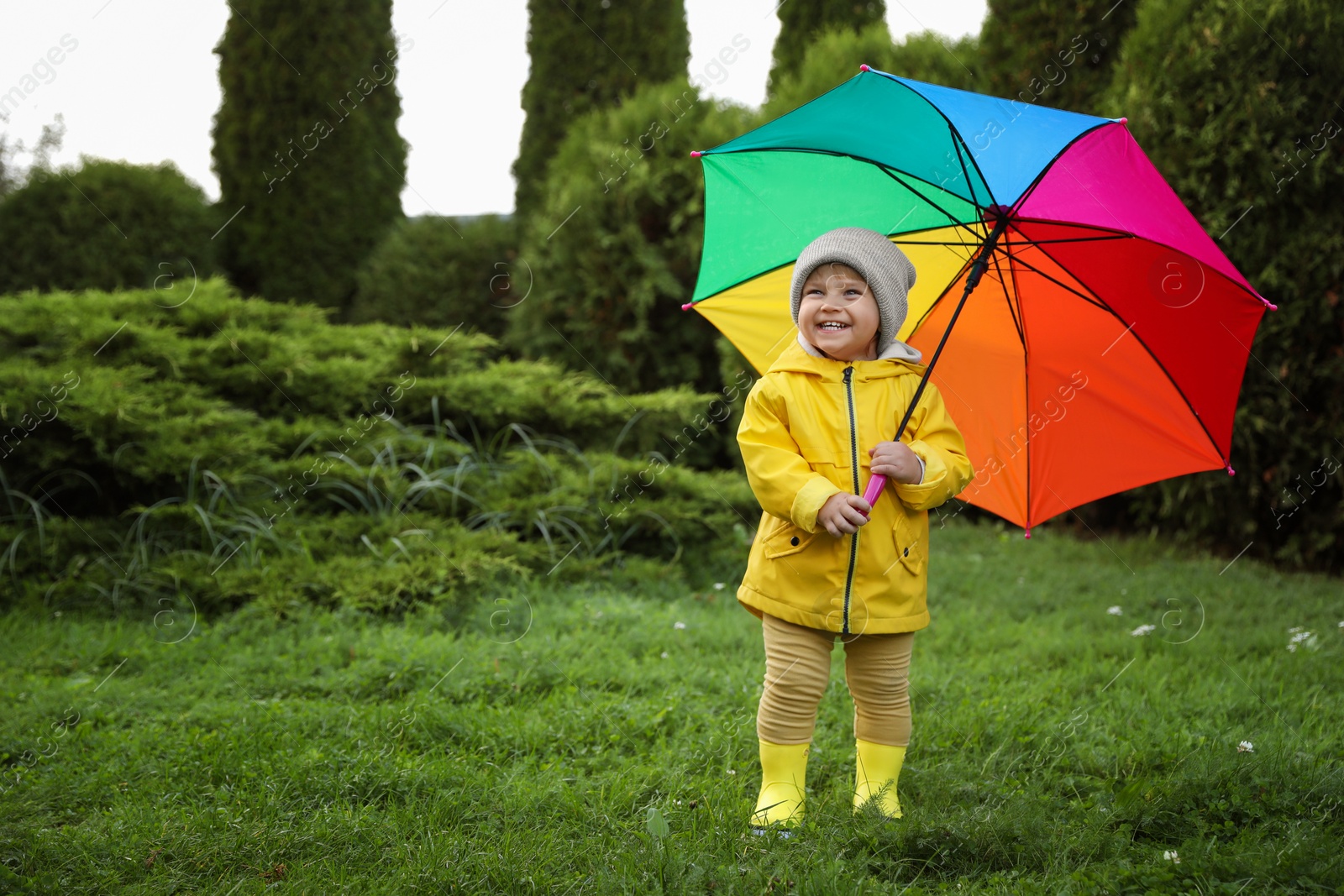 Photo of Cute little girl holding colorful umbrella in garden, space for text