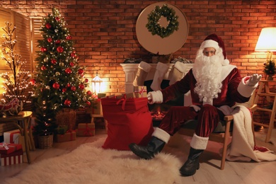 Photo of Santa Claus with sack of gifts in armchair at home