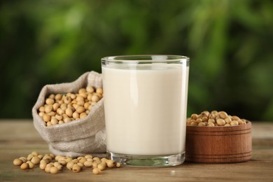 Photo of Glass with fresh soy milk and grains on white wooden table against blurred background