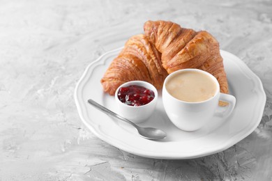 Photo of Tasty breakfast. Cup of coffee, fresh croissants and jam on grey table, space for text