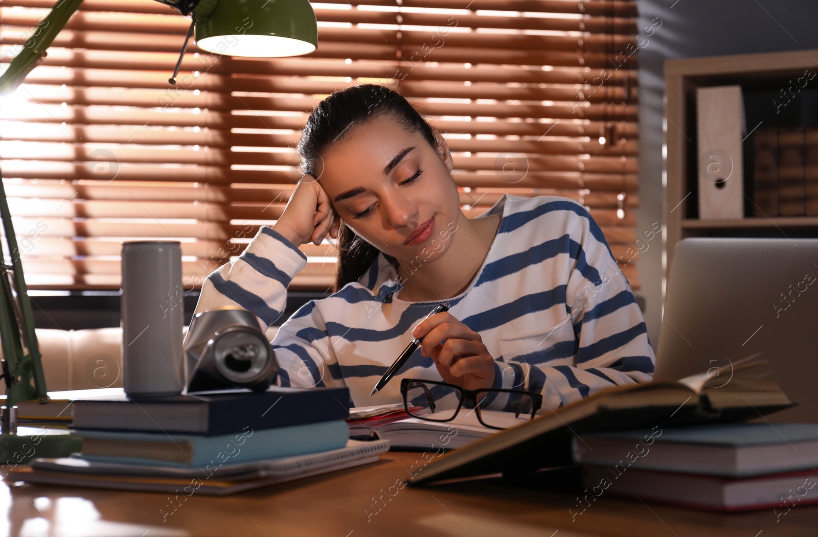 Photo of Tired young woman with energy drink studying at home