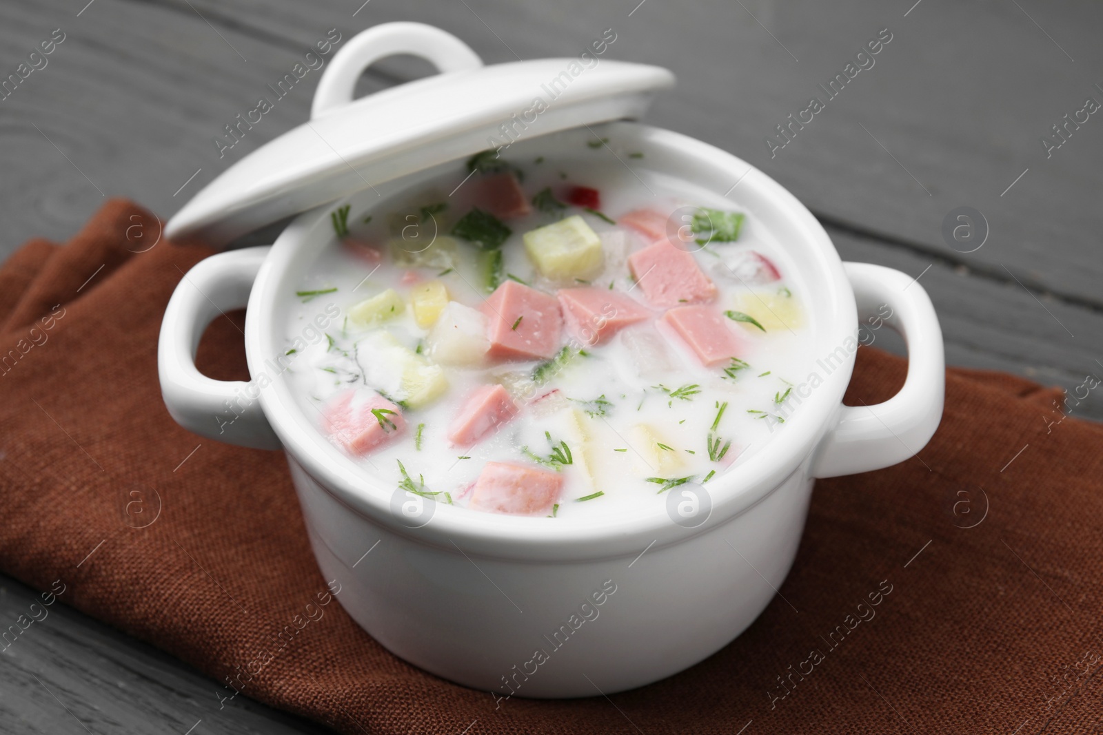 Photo of Delicious cold summer soup (okroshka) with boiled sausage in pot on grey table, closeup