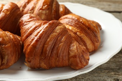 Plate with tasty croissants on wooden table, closeup