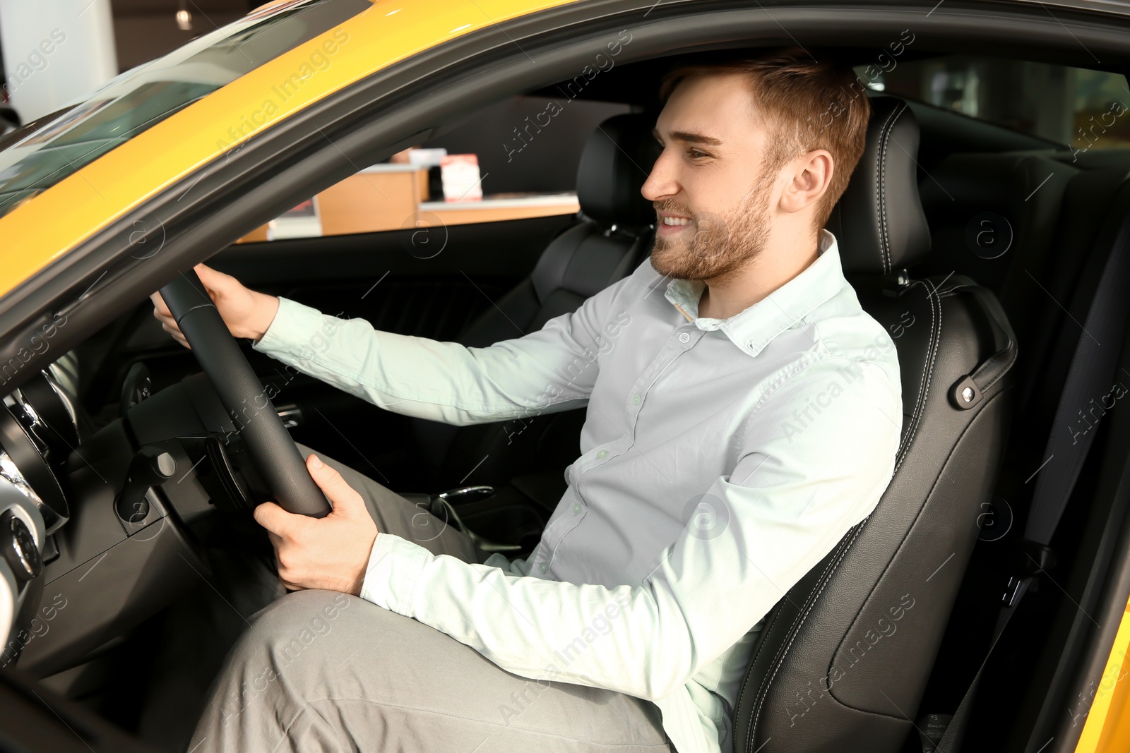 Photo of Young man sitting in driver's seat of new car at salon