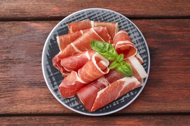 Photo of Plate with rolled slices of delicious jamon and basil on wooden table, top view