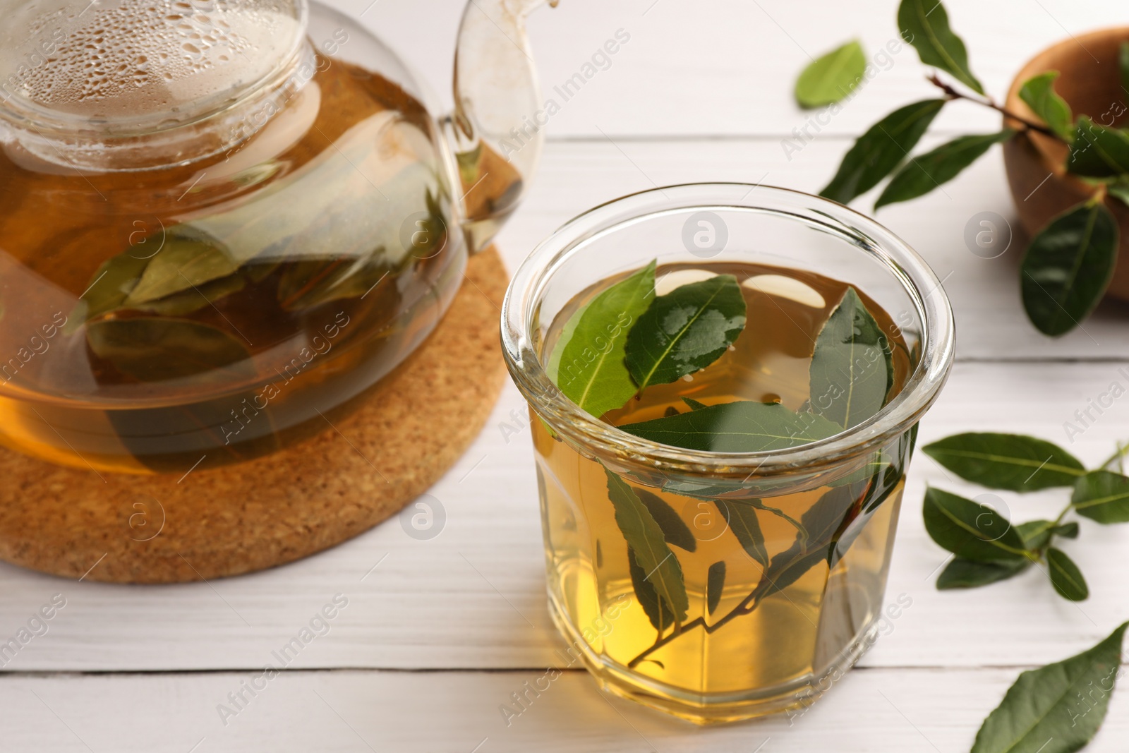 Photo of Cup of freshly brewed tea, teapot and bay leaves on white wooden table, closeup