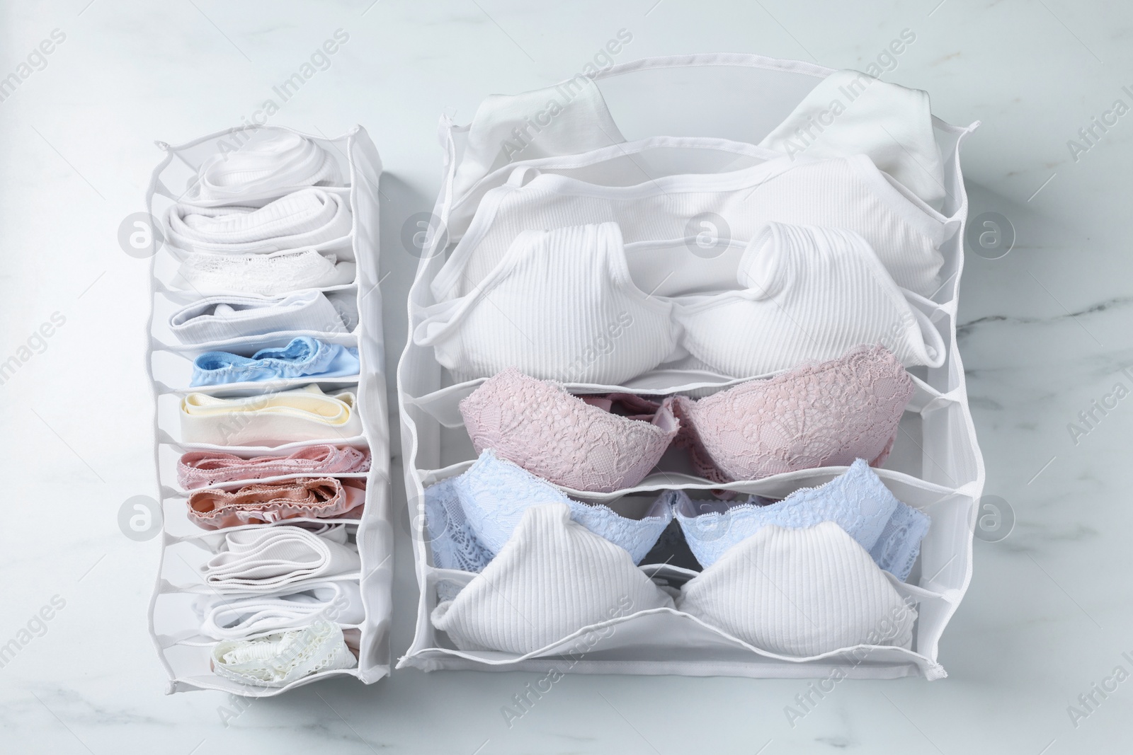 Photo of Organizers with folded women's underwear on white marble table, flat lay