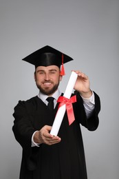 Happy student with graduation hat against grey background, focus on diploma